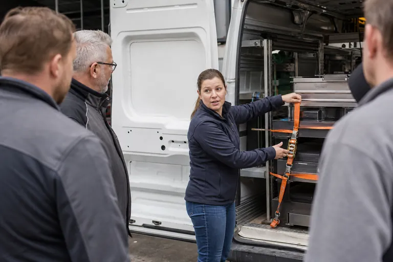 Fuhrparkverantwortliche unterweist Fahrer zur Ladungssicherung an einem Lieferwagen.